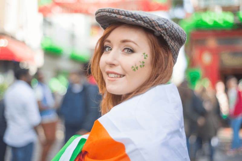 Woman with shamrock leaf design on her cheek with Irish flag on her shoulders