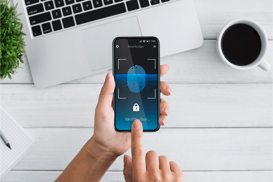 Person unlocking smartphone with fingerprint on wooden desk